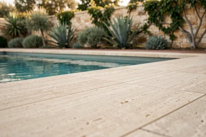 Margelles de piscine en travertin naturel beige au bord d'une piscine extérieure moderne entourée de plantes méditerranéennes